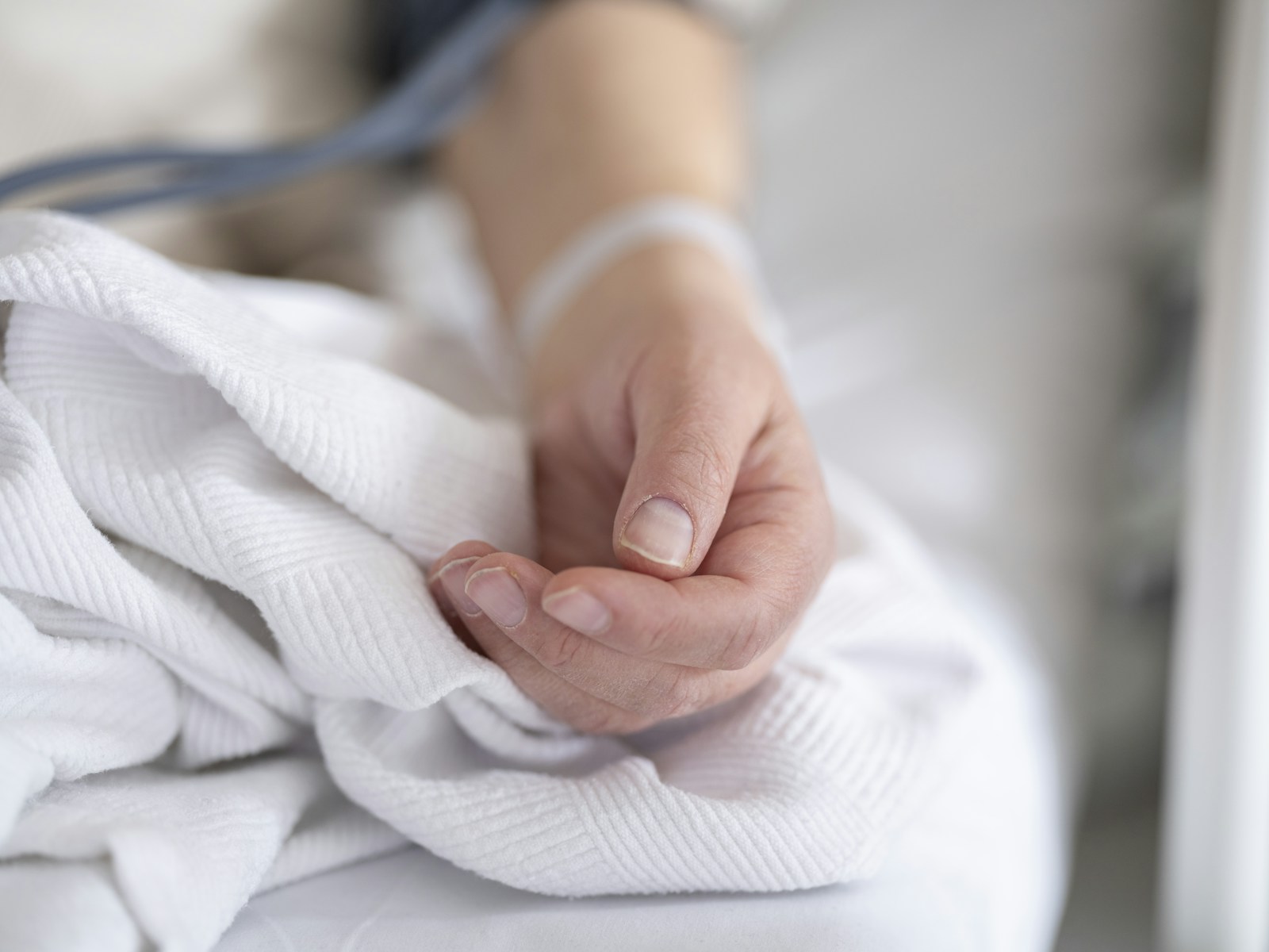 A single hand resting naturally on a clean white hospital blanket